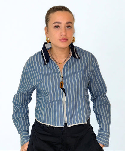 Striped Edge Shirt by Chez Neeba — cropped long-sleeve striped shirt featuring a ripped edge finish, full front zip with a camel leather pull, and a contrasting navy-blue textured collar with white details for a bold, modern statement look.
